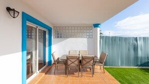 Une terrasse avec une table et des chaises, une porte-fenêtre coulissante et une vue sur une pelouse verdoyante.