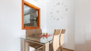 Un coin repas comprenant une table en verre, des chaises en bois, un miroir avec un cadre en bois et une horloge murale.