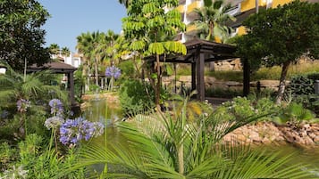 A garden with a pond, palm trees, and a pergola.