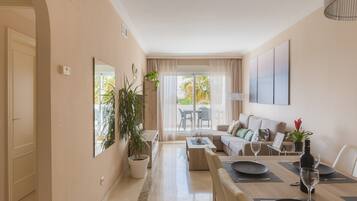 A modern living room with a dining area, a sofa set, and a large window with curtains.