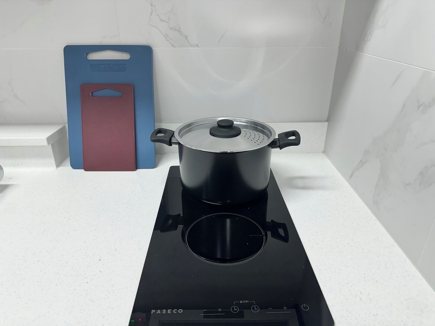 A kitchen with a stove, a pot, and a blue and red kitchen tool on the counter.