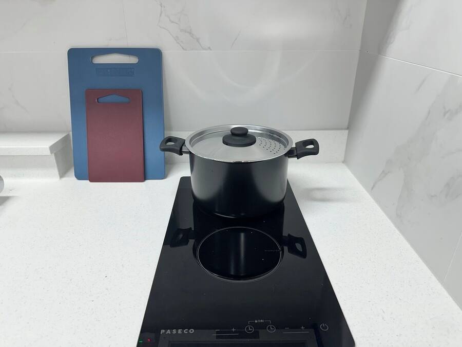 A kitchen with a stove, a pot, and a blue and red kitchen tool on the counter.