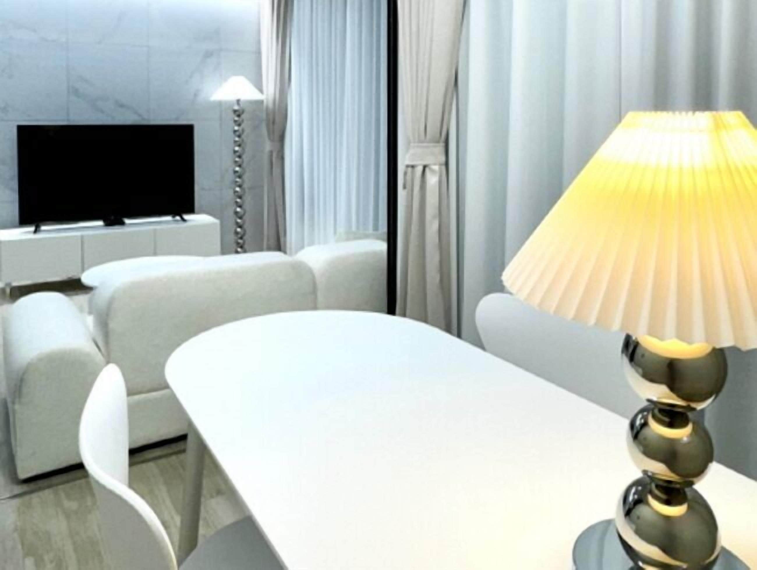 A modern living room with a flat-screen TV, a sofa, a dining table, and a lamp.