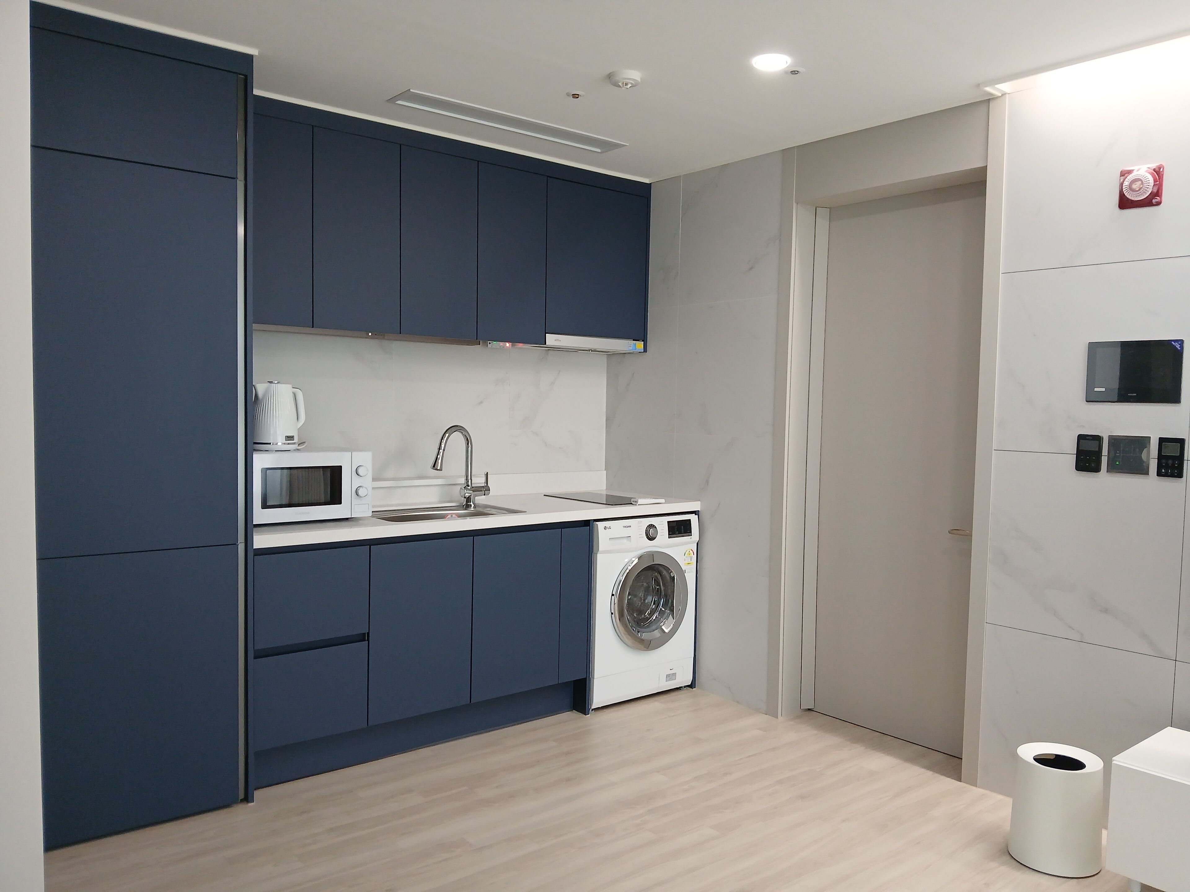 A modern kitchen with dark blue cabinets, a white countertop, a microwave, a sink, and a washing machine.
