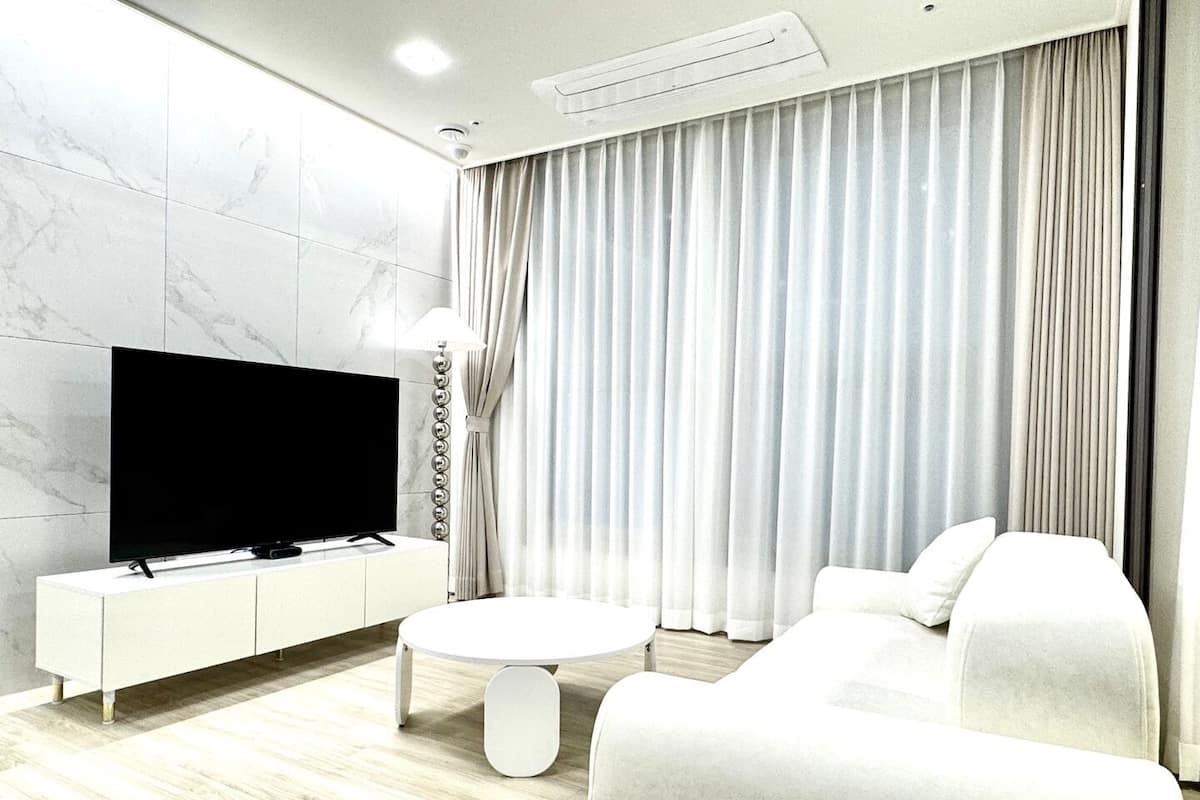 A modern living room with a flat-screen TV on a white console, a round coffee table, and a white sofa.