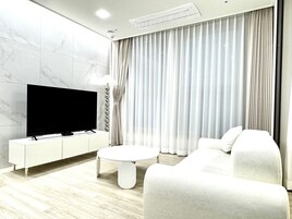 A modern living room with a flat-screen TV on a white console, a round coffee table, and a white sofa.