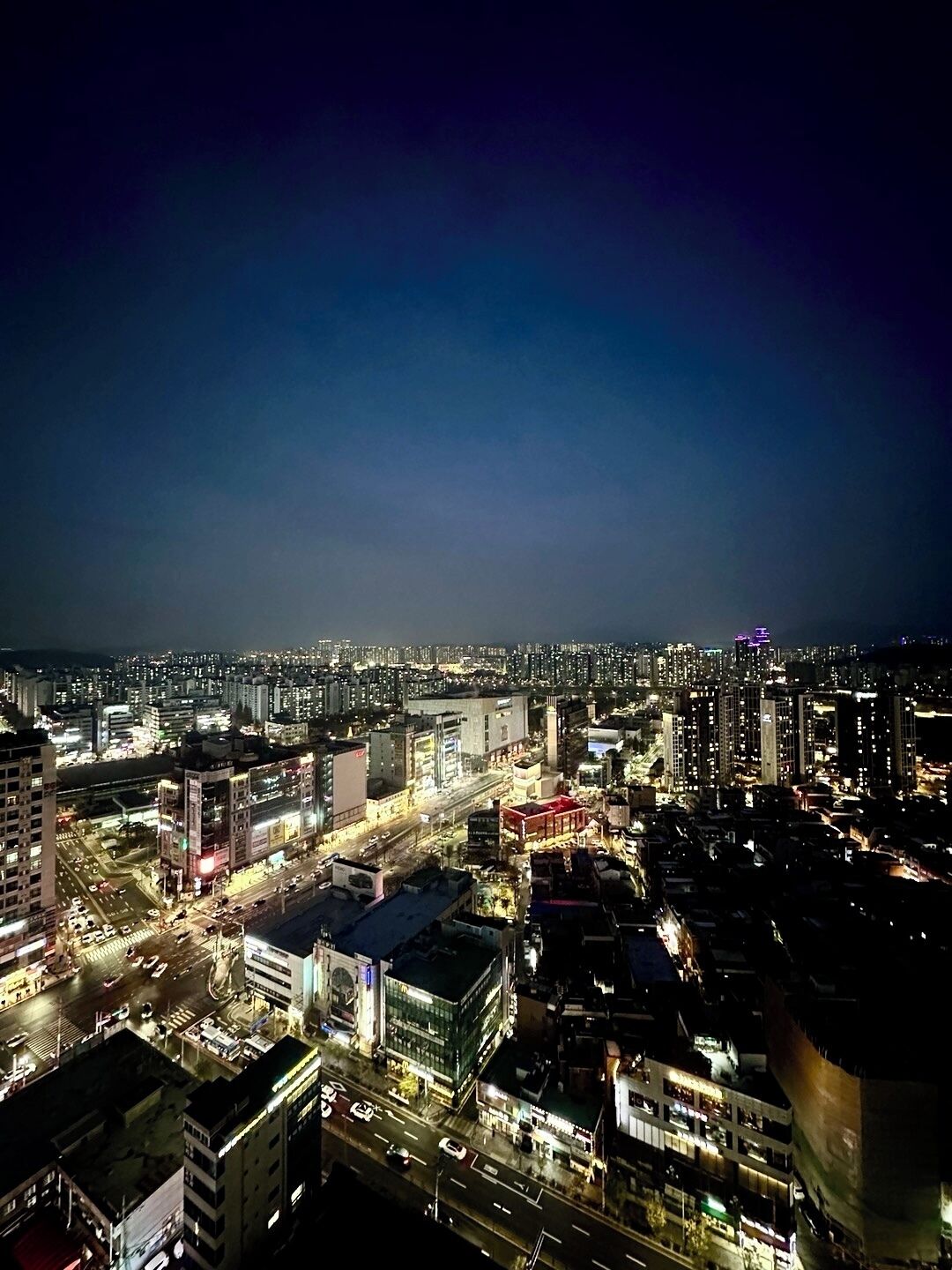 A nighttime cityscape with high-rise buildings, illuminated streets, and a prominent building with a red roof in the foreground.