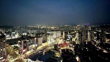 A nighttime cityscape with high-rise buildings, illuminated streets, and a prominent building with a red roof in the foreground.