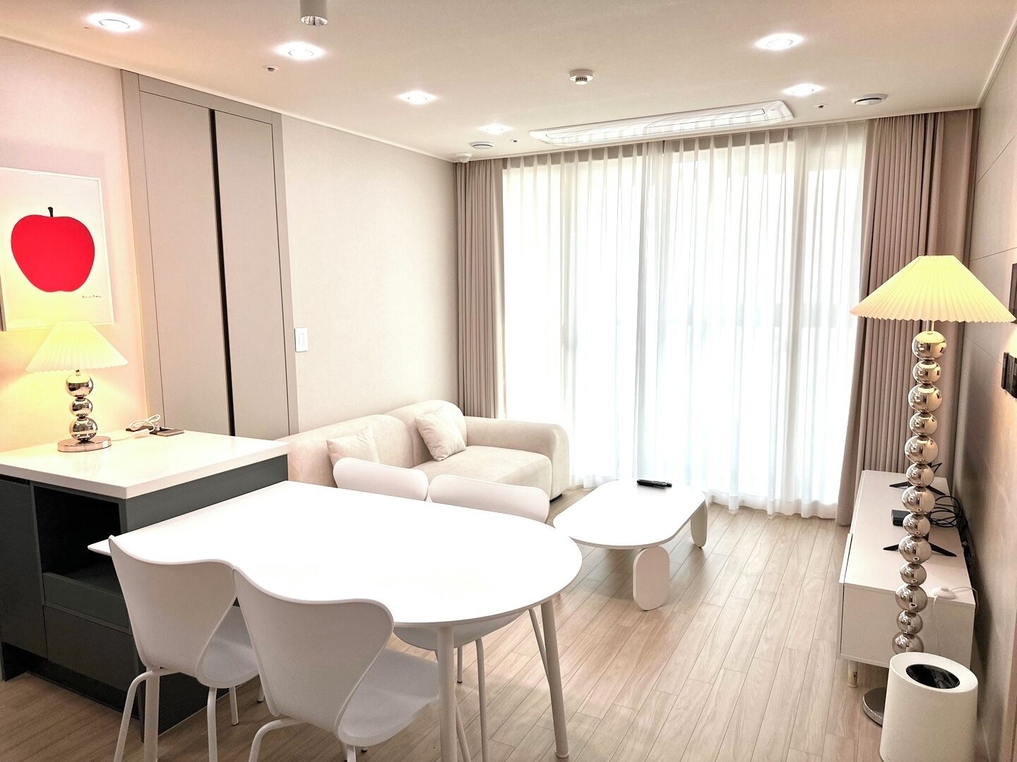 Ein modernes Hotelzimmer mit einem weißen Sofa, einem Esstisch mit Stühlen, einem kleinen Couchtisch und einer Lampe.