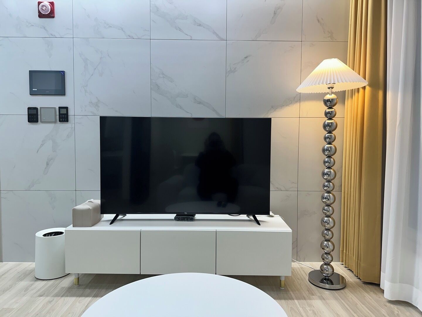 A modern living room with a flat-screen TV on a white cabinet, a floor lamp, and a toilet paper holder.