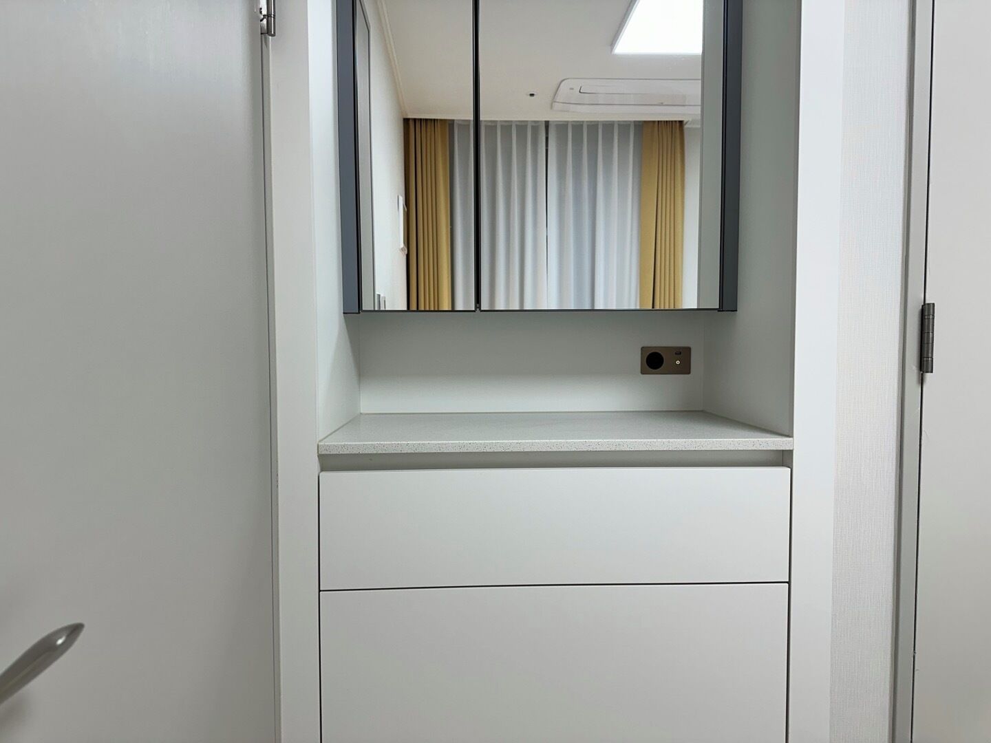 A white wardrobe with a mirror above it, a small shelf, and a door with a handle.