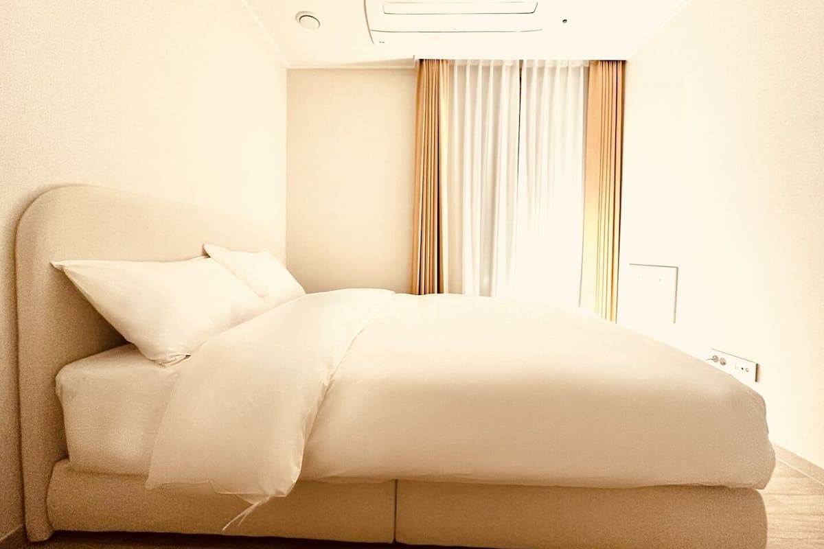 A modern bedroom with a bed, curtains, and a wall-mounted air conditioner.