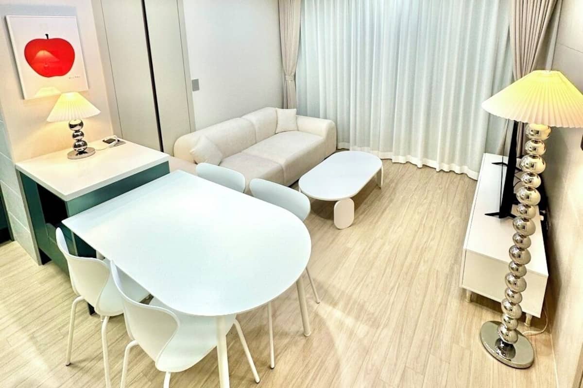 A modern, well-lit room with a dining area, a sofa, and a lamp.