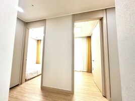 A narrow hallway with wooden flooring and white walls, leading to two rooms with beds and curtains.
