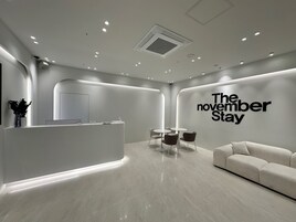 A modern reception area with a reception desk, seating area, and a wall with the text "The November Stay".