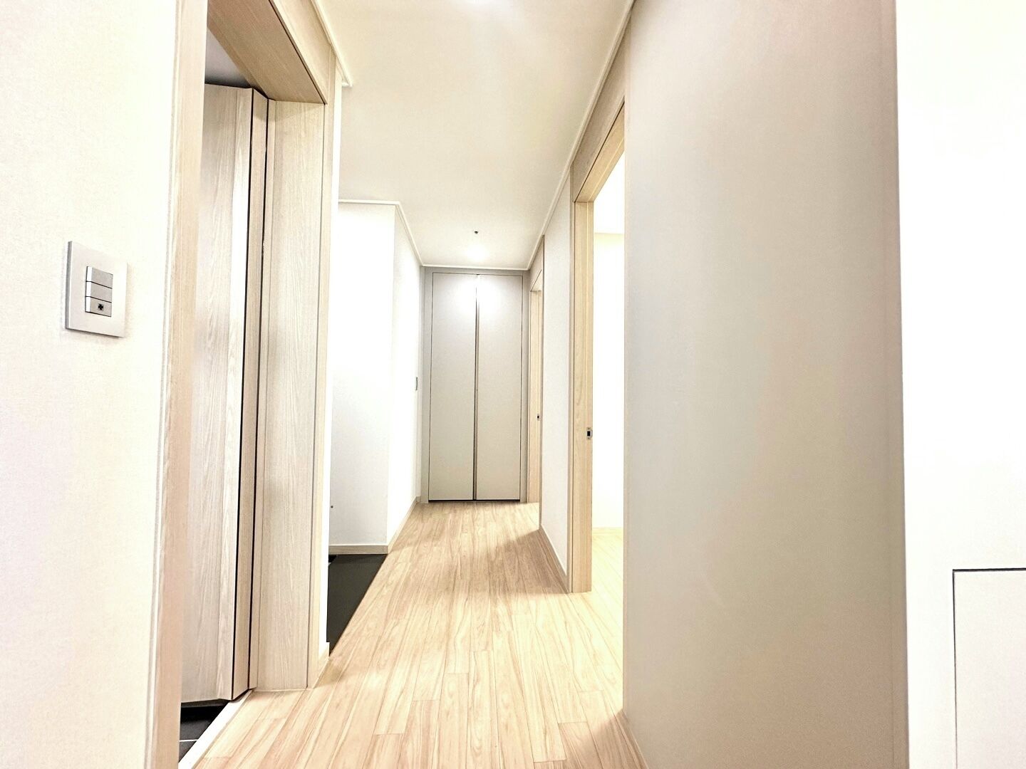 Un pasillo estrecho con suelo de madera, paredes blancas y una puerta al final.