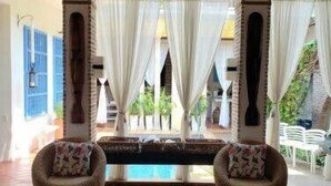 A room with a pool, two wicker chairs with floral cushions, and a view of greenery outside. - w *| Sensational 4BR House w/ pool in Cartagena (Cartagena de Indias)