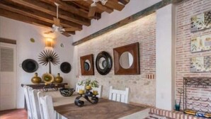 A dining area with a rustic wooden table and white chairs, a brick wall with decorative plates, and a ceiling fan. - w *| Sensational 4BR House w/ pool in Cartagena (Cartagena de Indias)