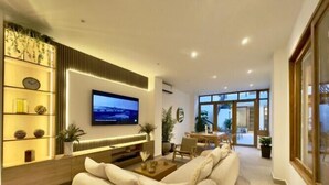 Ein modernes Wohnzimmer mit einer großen Couch, einem an der Wand befestigten Flachbildfernseher und einem Essbereich mit Tisch und Stühlen.