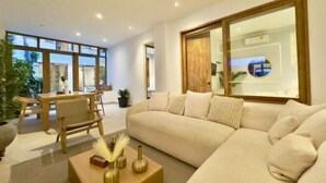 Ein modernes Wohnzimmer mit einem großen Ecksofa, einem Couchtisch aus Holz mit Dekoration und einem Essbereich mit Holztisch und Stühlen.