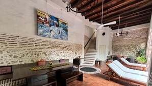 A spacious living area with a wooden bench, a dining table, and a lounge area with two sunbeds. A staircase leads to an upper level, and a painting is visible on the wall. - w* |Marvelous 3BR House with pool in Cartagena (Cartagena de Indias)