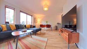 A modern living room with a sofa, coffee table, TV, and dining area. - The Eastside Escape! Stunning 2 Bed Walk Anywhere (Belfast)