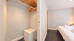 A bedroom with a bed, a bedside table, a hanging clothes rack, and a door leading to another room.
