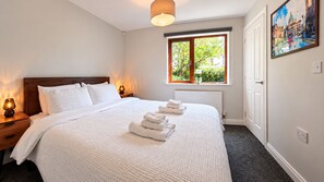 Hotellihuone, jossa on suuri sänky, ikkuna, josta avautuu näkymä vehreään maisemaan, taulu seinällä ja yöpöytälamppu.