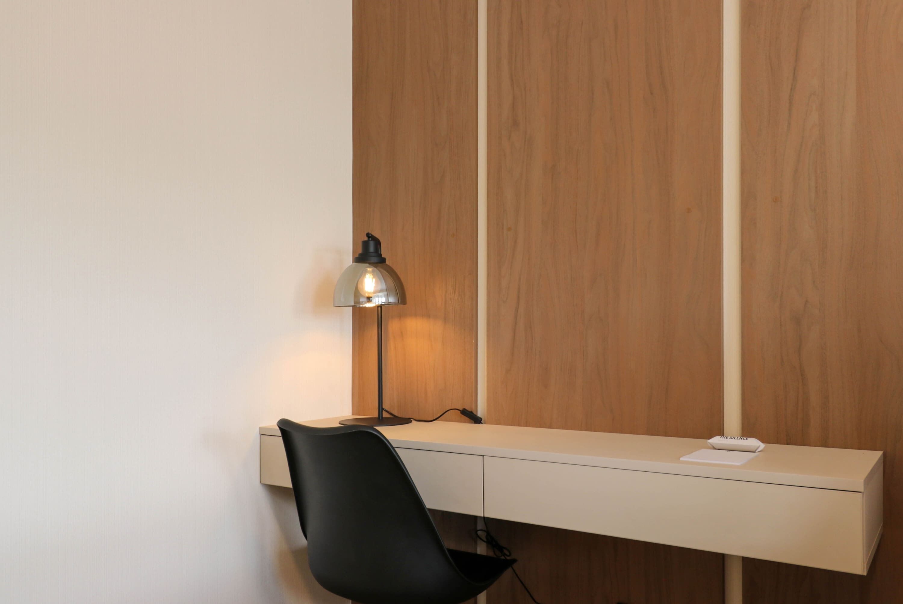 A modern desk with a lamp, a chair, and a wooden panel wall.