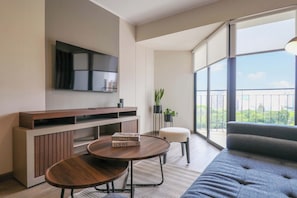 A modern living room with a sofa, a coffee table, a TV mounted on the wall, and a balcony with a view.