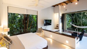 Een moderne slaapkamer met een groot bed, een televisie en uitzicht op weelderige begroeiing.