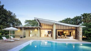 Una casa moderna con piscina, mobiliario de exterior y fachada de piedra.