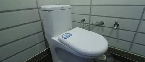 Eine weiße Toilette mit einem blauen Aufkleber, einem chromfarbenen Wasserhahn und einer gefliesten Wand.