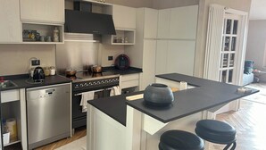 A modern kitchen with a built-in oven, a coffee maker, and a kettle on the counter. There is a small island with stools and a vase. - Garibaldi 14 Suite (Chianciano Terme)