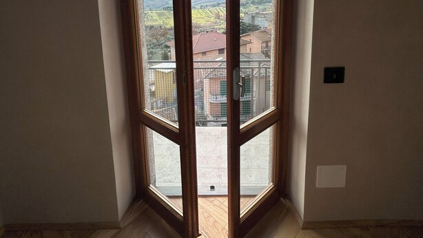 A room with a large, open wooden door leading to a balcony. The room has a herringbone-patterned wooden floor and plain white walls. - Garibaldi 14 Suite (Chianciano Terme)
