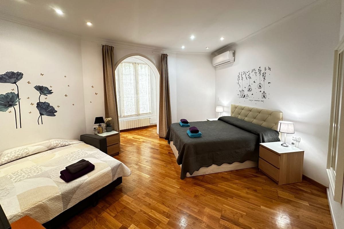 A bedroom with a bed, a nightstand, a dresser, a window with curtains, and a wall decoration.
