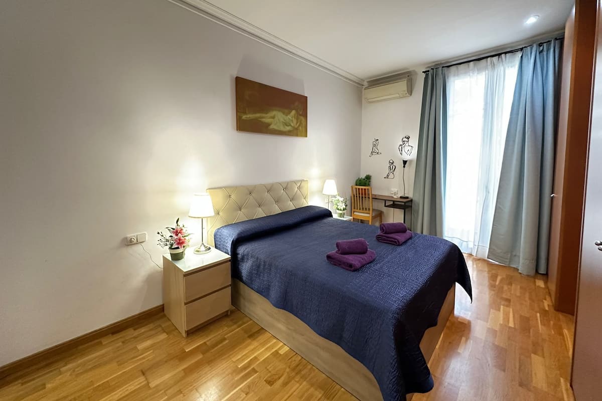 A hotel room with a bed, bedside tables, a desk, and a window with curtains.