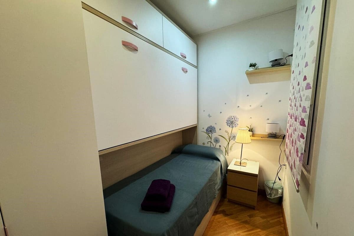 A small bedroom with a single bed, a nightstand, a lamp, and a wardrobe.