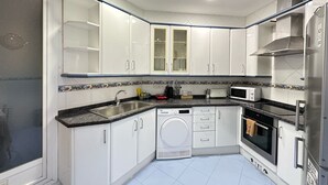 Una cocina moderna con armarios blancos, horno integrado, microondas y lavavajillas.