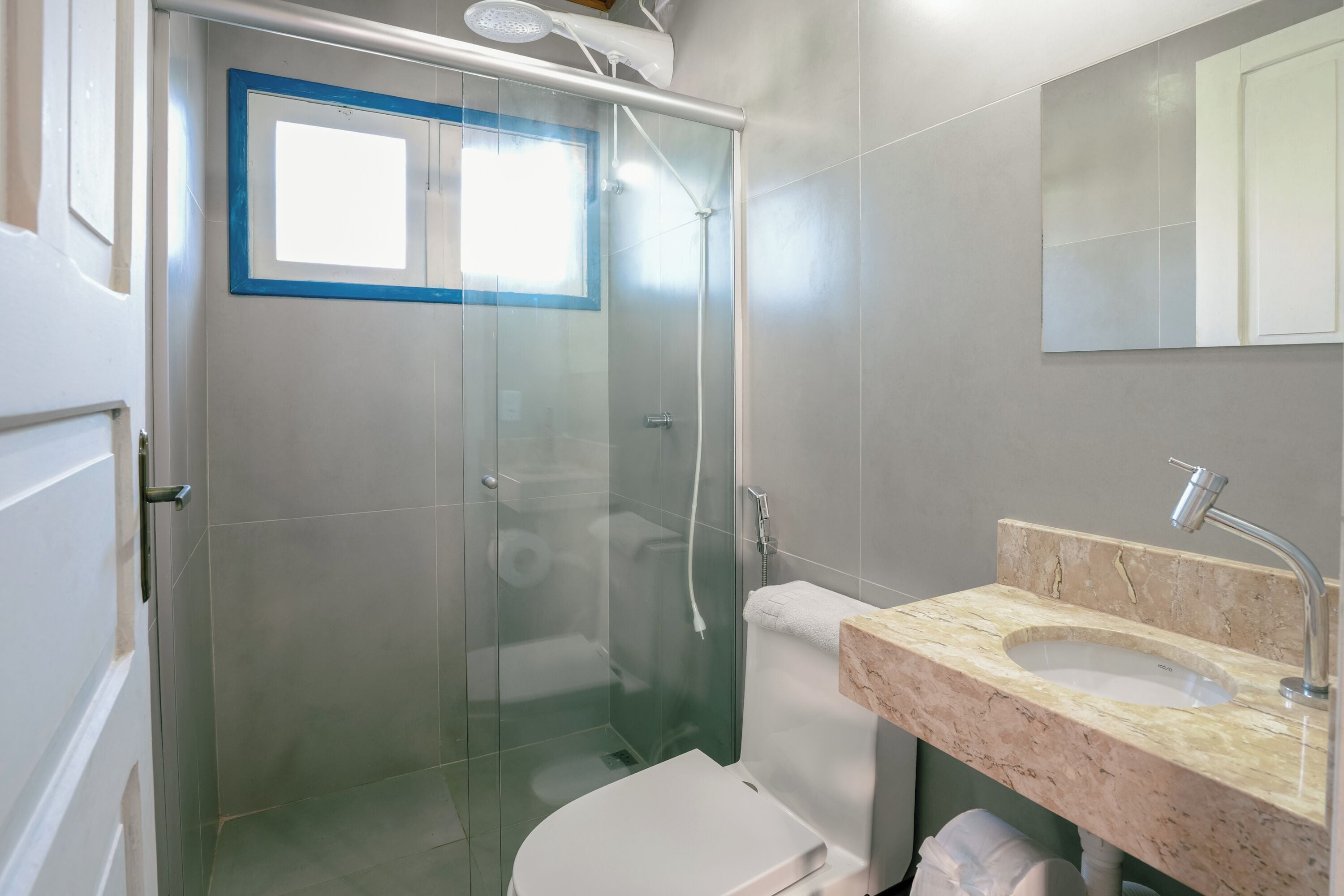 Een moderne badkamer met een douchecabine van glas, een wit toilet en een marmeren wastafel.
