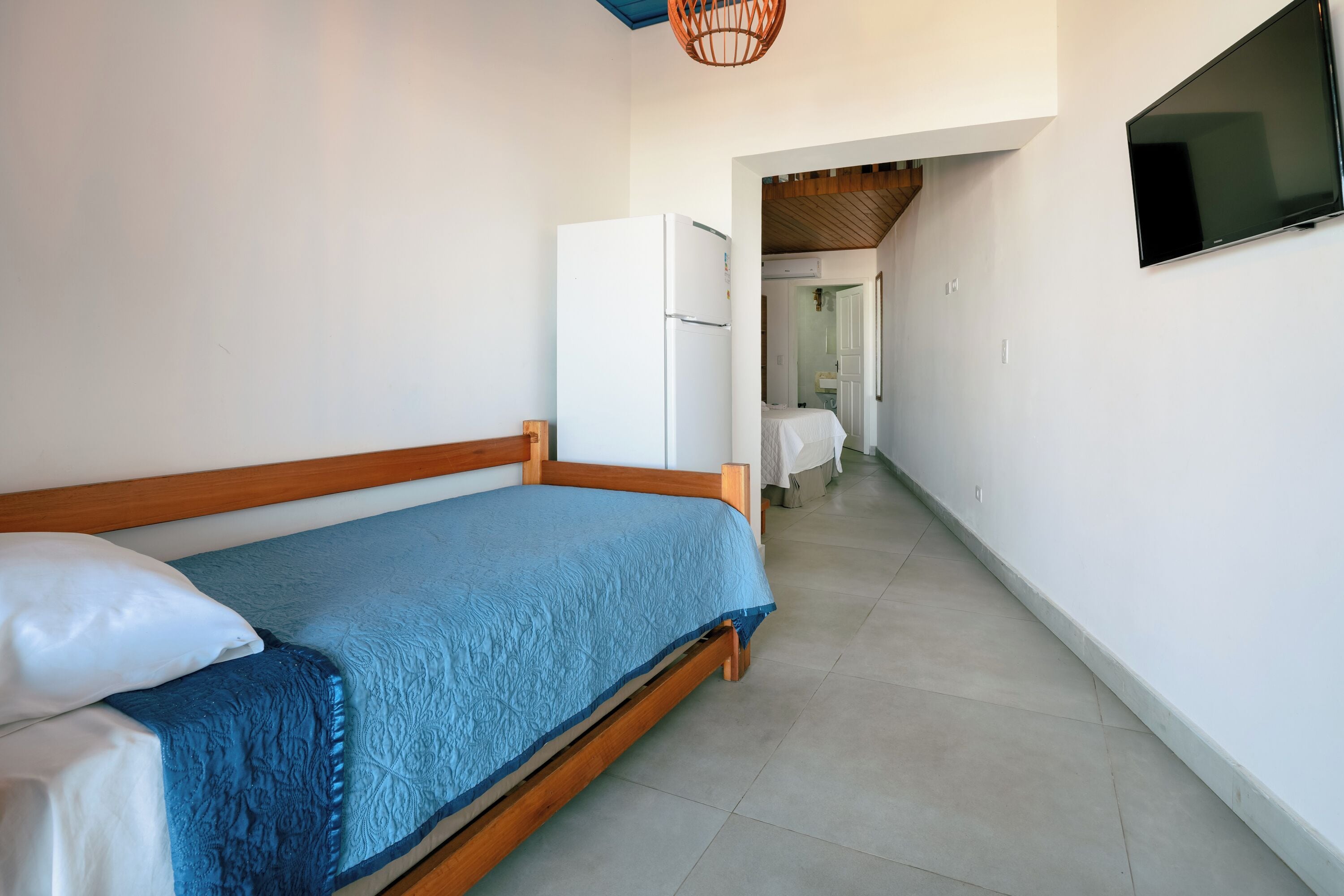 A bedroom with a wooden bed, a white refrigerator, and a TV mounted on the wall.