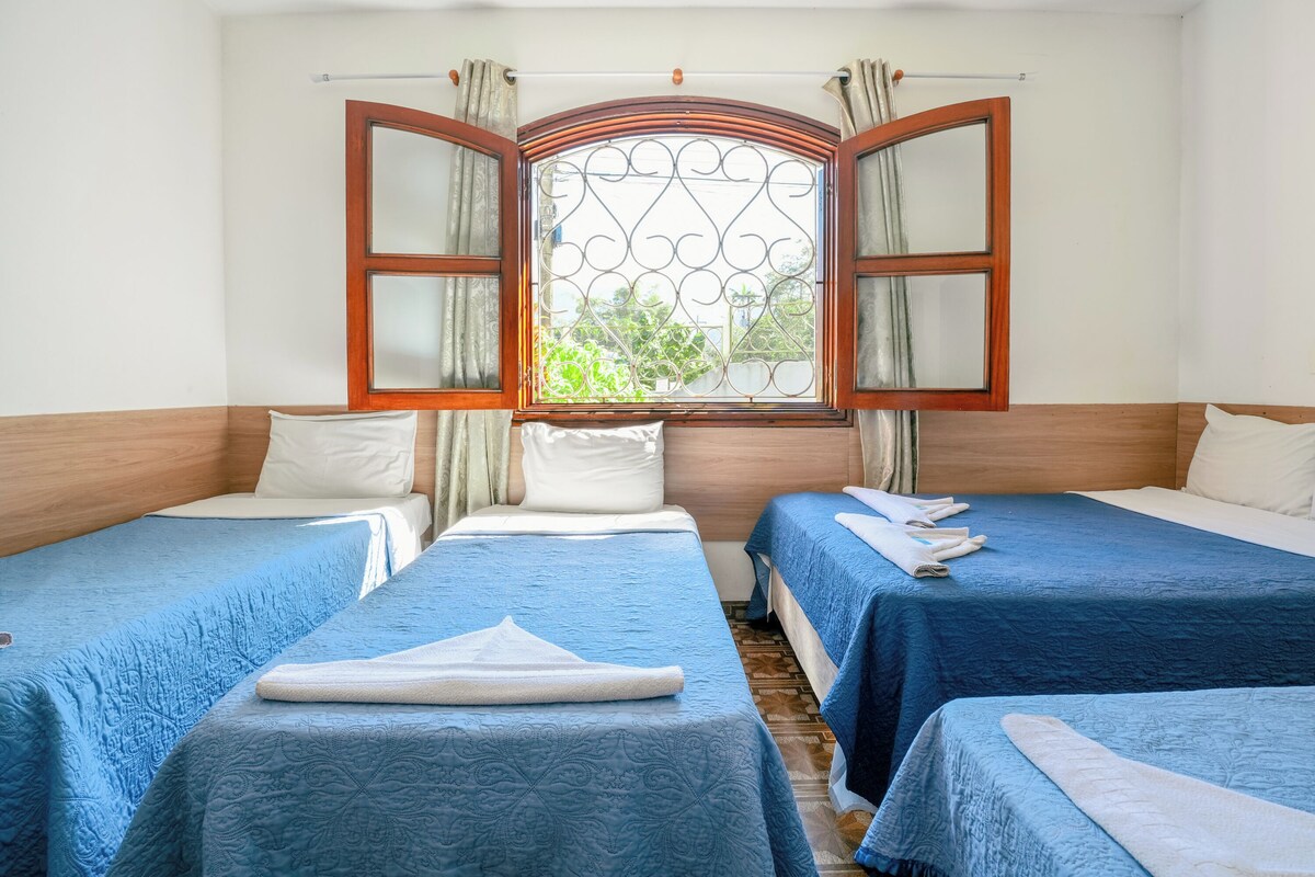 A room with two beds, a window with curtains, and a wooden headboard.
