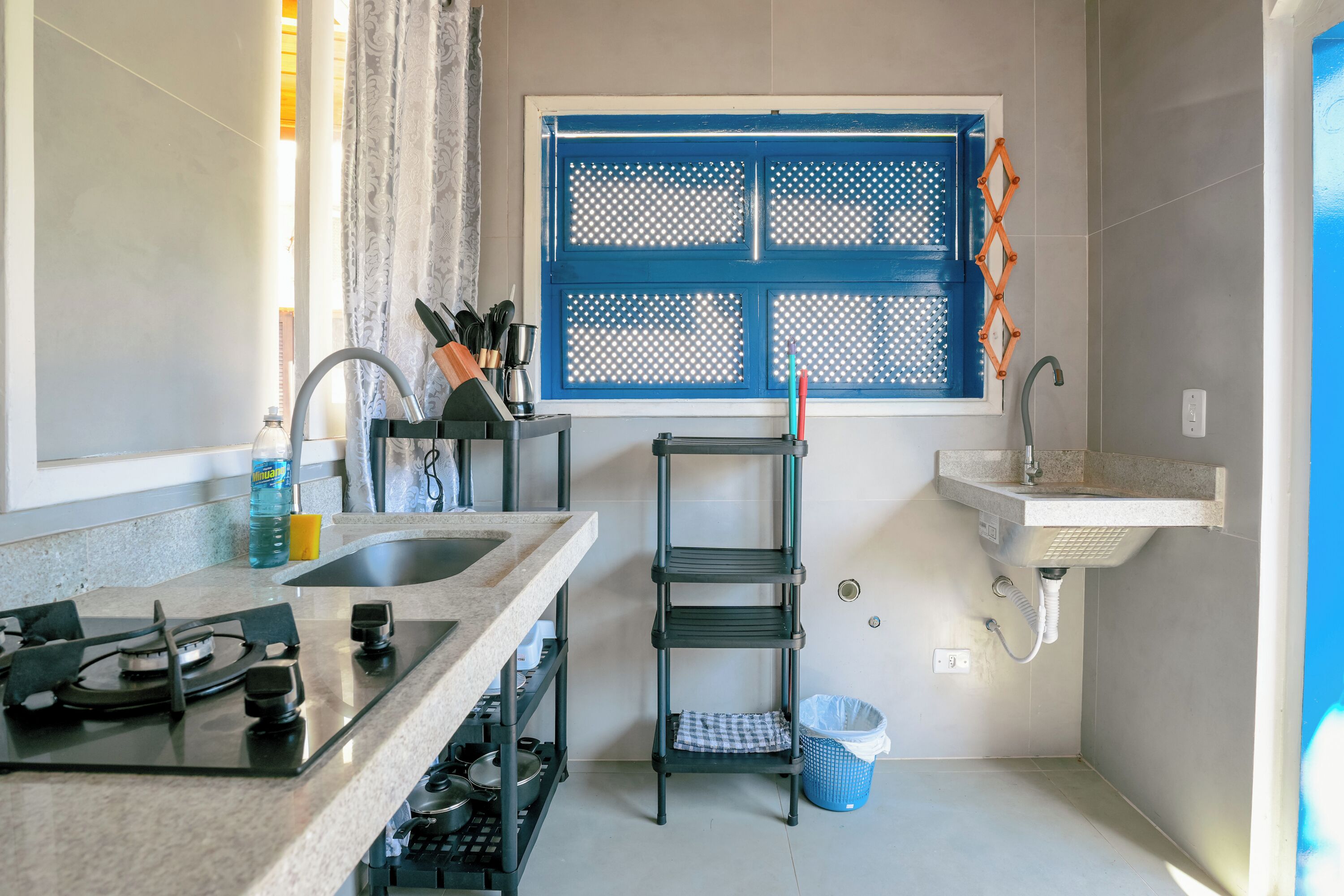 A compact kitchen with a gas stove, a sink, and a window with blue shutters.