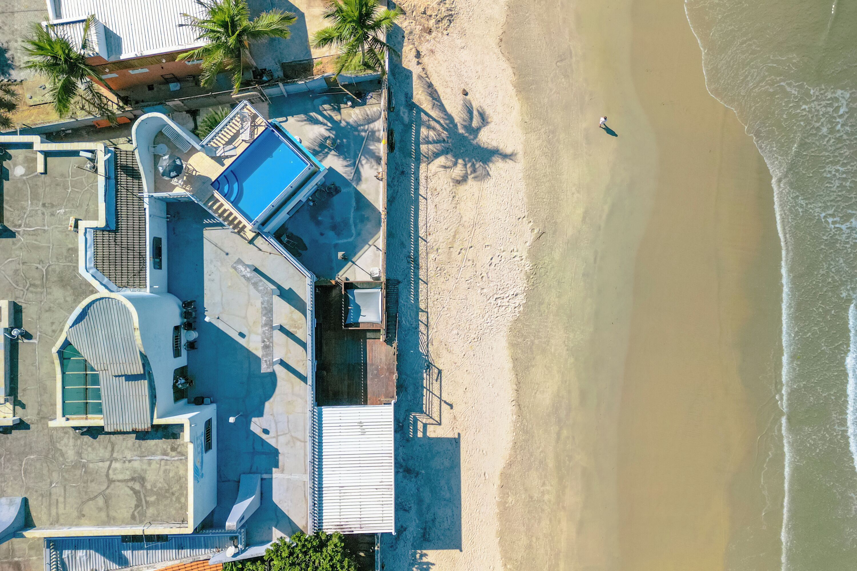 Luchtbeeld van een pand aan het strand met een zwembad, een overdekt terras en een strandgedeelte.