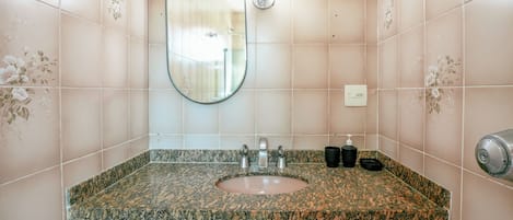 A bathroom with a granite countertop sink, a mirror, a soap dispenser, and a towel dispenser.