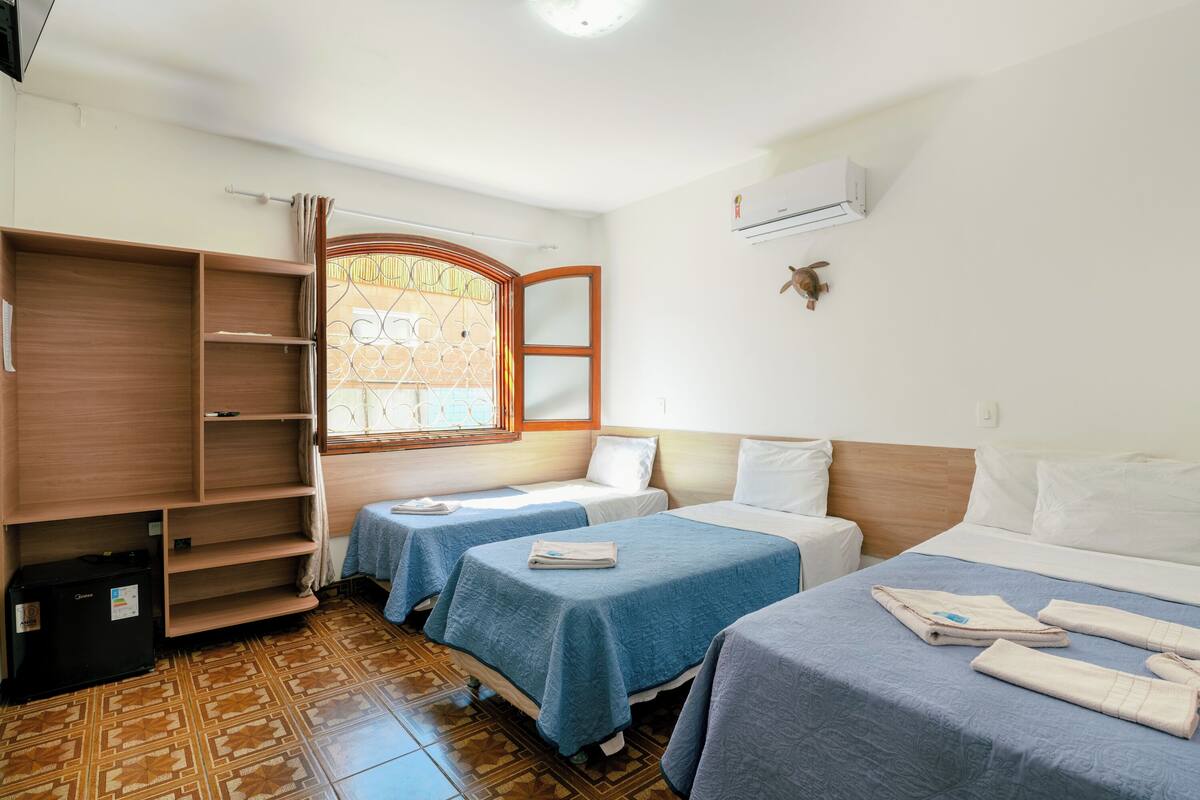 Une chambre d’hôtel avec deux lits simples, une armoire, une petite table et une fenêtre donnant sur un beau paysage.