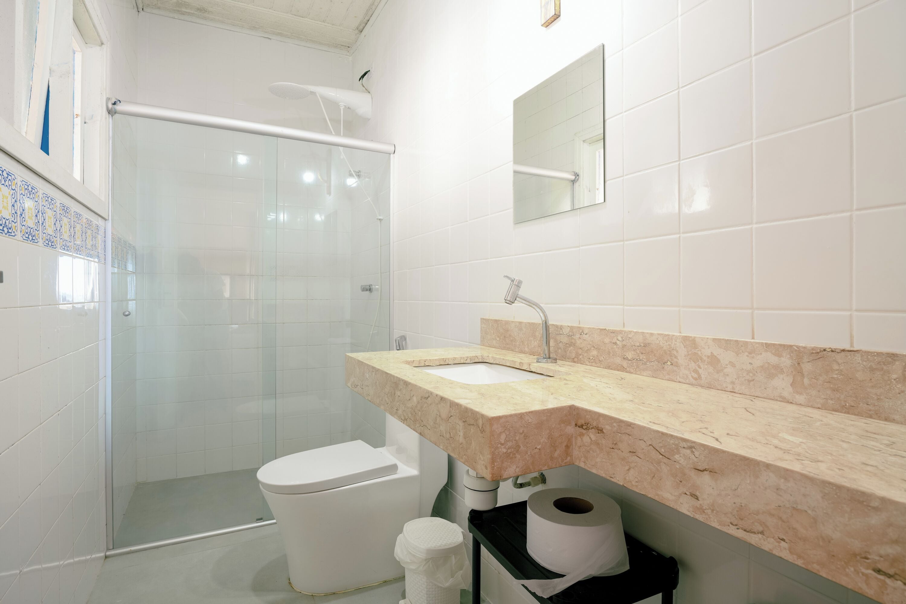 A bathroom with a glass shower enclosure, a toilet, a sink with a beige countertop, and a mirror above the sink.