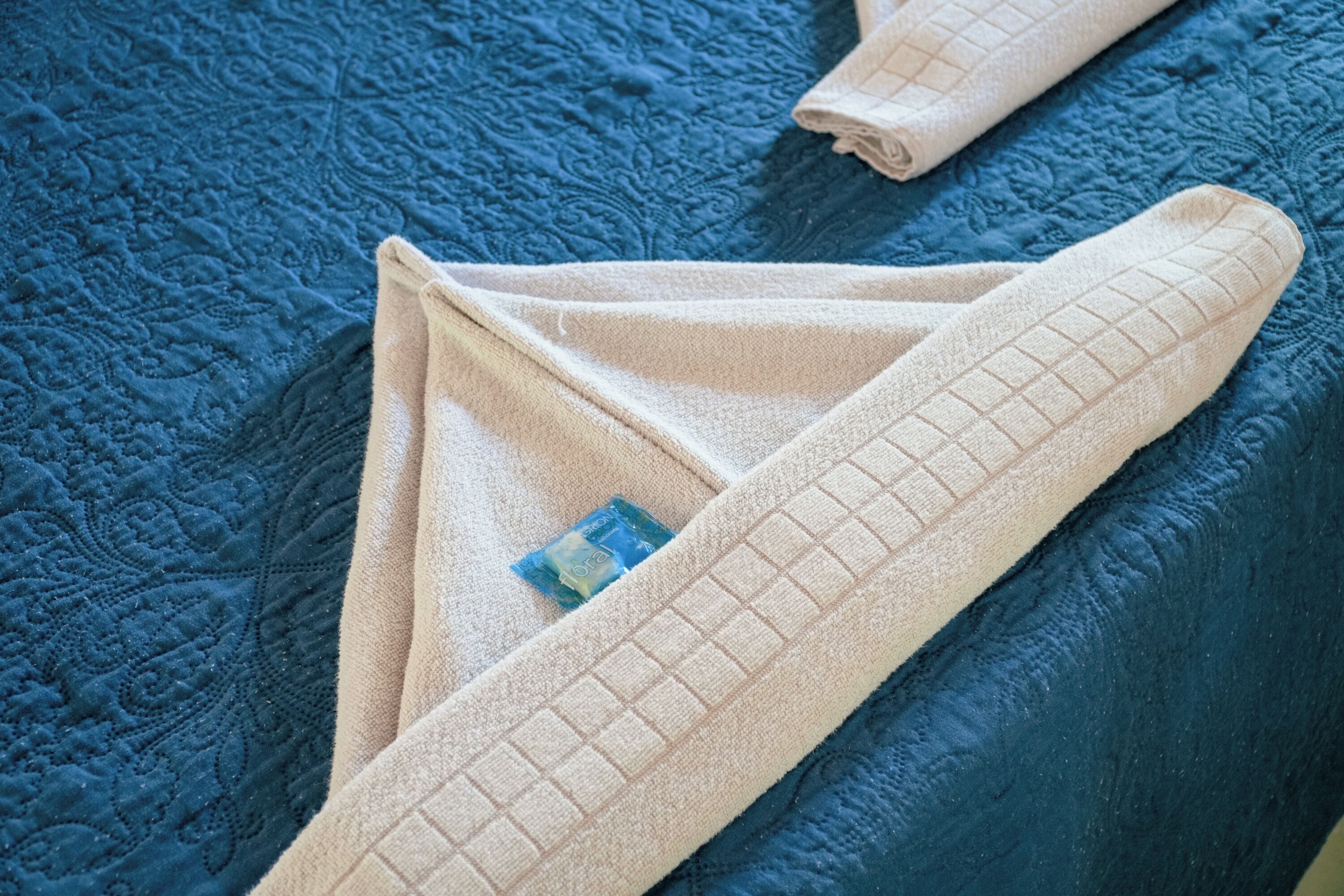 A bed with a blue quilt and a beige towel with a grid pattern.
