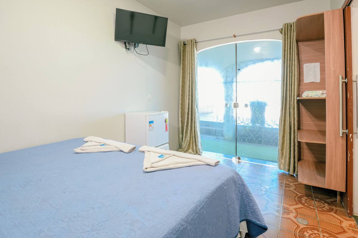 Une chambre comprenant un lit, un téléviseur fixé au mur, un petit réfrigérateur et une armoire en bois.