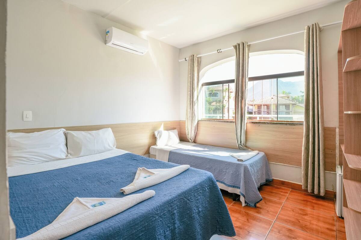 Une chambre d’hôtel avec deux lits, une fenêtre avec des rideaux, un appareil de climatisation et une vue sur les bâtiments environnants.